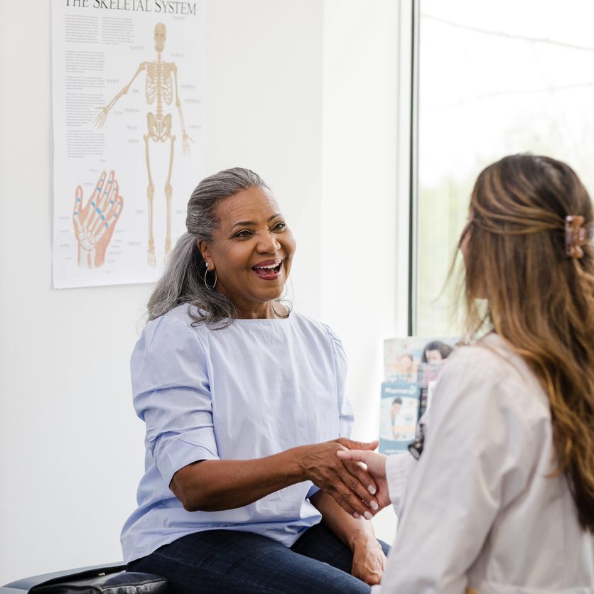 The mature woman smiles while shaking hands with the female healthcare professional as she introduces herself.